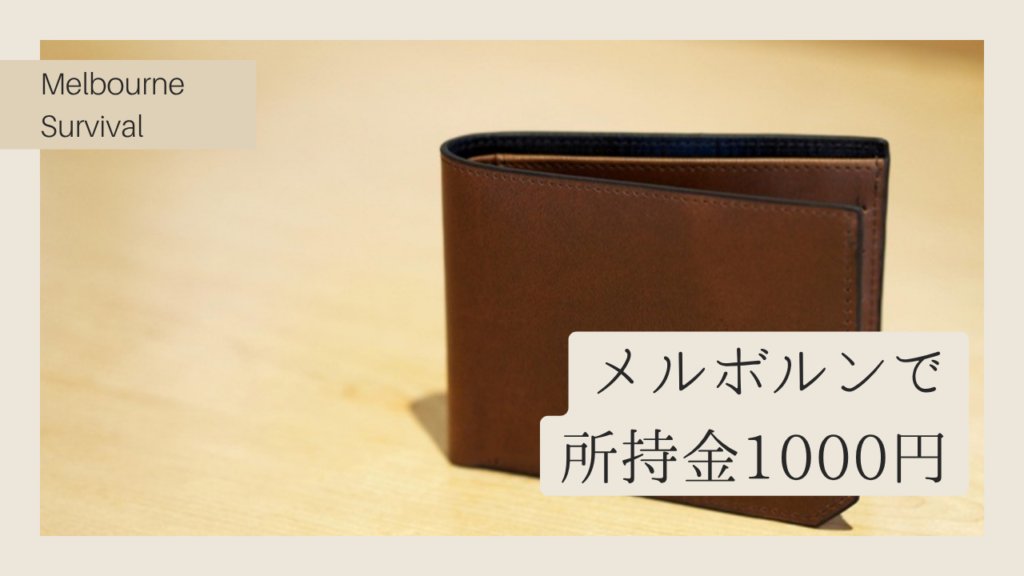 木製テーブルに置かれた茶色い革の財布と「メルボルンで所持金1000円」のテキスト